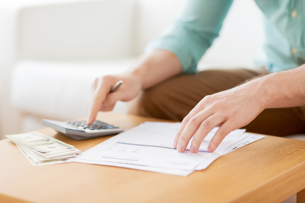 savings, finances, economy and home concept - close up of man with calculator counting money and making notes at home