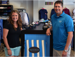 Man and woman standing in store; scrubs hanging on clothes ranks behind them