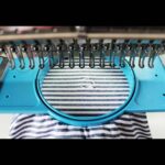 Close‑up of an embroidery machine stitching a small white logo onto blue‑and‑white striped fabric held in a circular hoop.