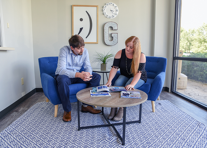 Man and woman, sitting on chairs, look through a stack of brochures on a coffee table in front of them.