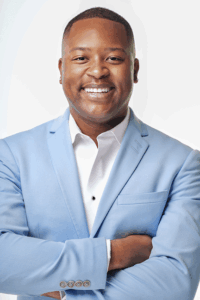 Person wearing a light blue blazer over a white dress shirt, standing with arms crossed against a plain white background.
