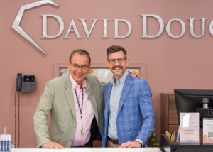 Two people stand behind a jewelry store display counter beneath a large "David Douglas" wall sign.
