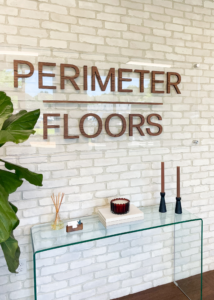 Perimeter Floors office lobby featuring the company logo mounted on a white brick wall above a glass table with decorative accents and plants.
